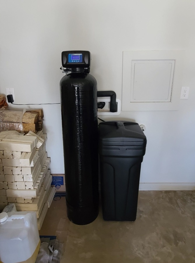 Outdoor water softener installation beside a brick home