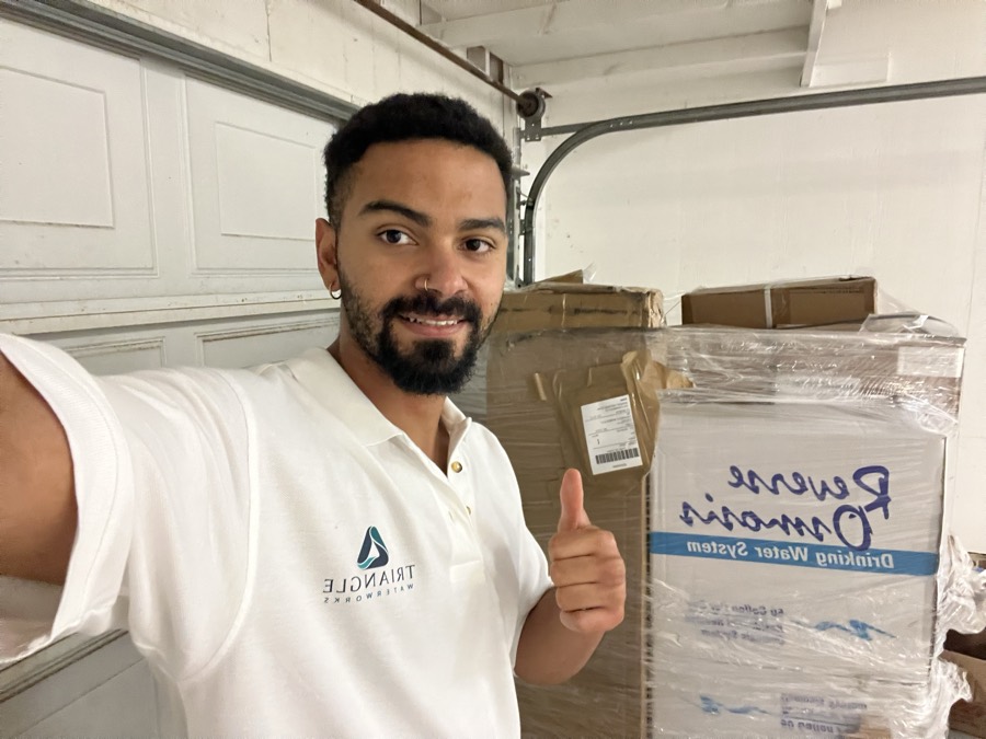 Triangle Waterworks owner giving a thumbs up next to reverse osmosis systems in stock